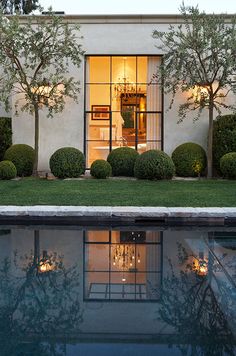 a house with a pool in front of it and trees around the pool area at night