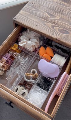 an open drawer filled with lots of different types of jewelry and hair accessories on top of a wooden table