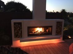 an outdoor fireplace lit up at night with the sun setting in the back ground behind it