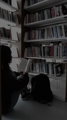 a person sitting on the floor reading a book in front of a bookshelf