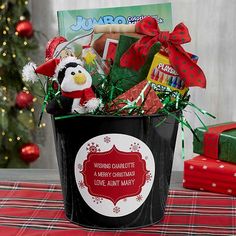 a red bucket filled with lots of holiday treats on top of a table next to a christmas tree