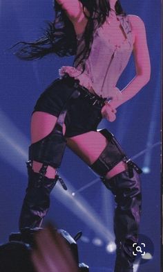 a woman in high boots is standing on stage with her legs spread out and she has long black hair