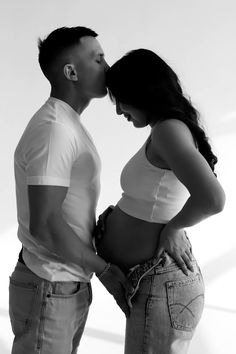 a man and woman kissing each other while standing in front of a white wall with their hands on their hips