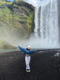 a woman standing in front of a waterfall with her arms spread wide out to the side