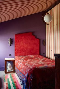 a bedroom with purple walls and a red headboard on the bed, next to a colorful rug