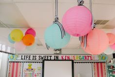 colorful paper lanterns hang from the ceiling above a classroom desk with posters and decorations on it