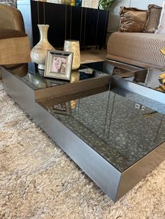 a coffee table with a glass top and metal frame on the bottom, sitting in front of a couch