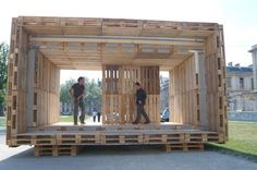 two men standing in the back of a large wooden structure made out of pallets