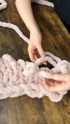 someone is crocheting something with yarn on a wooden table and another person is holding the yarn