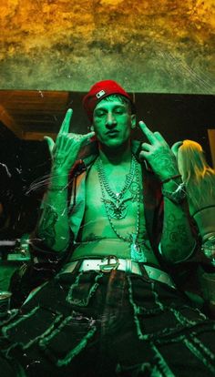 a man with green paint on his face sitting in front of a mirror and making the peace sign