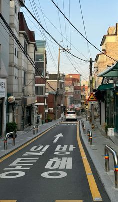 an empty city street with power lines above it and buildings on both sides, in the background