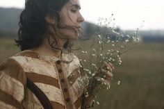 a woman standing in a field holding a bunch of white flowers and looking at the sky