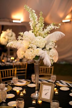 a tall vase filled with white flowers on top of a table covered in gold plates