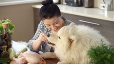 a woman petting a white dog on top of a wooden table next to vegetables