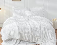 a bed with white comforter and pillows on top of wooden floor next to wall