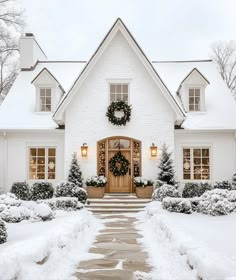 a white house covered in snow with wreaths on the front door