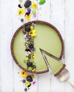 a cake decorated with flowers and berries on top of a white wooden table next to leaves