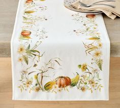 a white table runner with autumn flowers and pumpkins on it, sitting on a wood floor