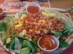 a plate full of salad and condiments with sauces on the side at a restaurant