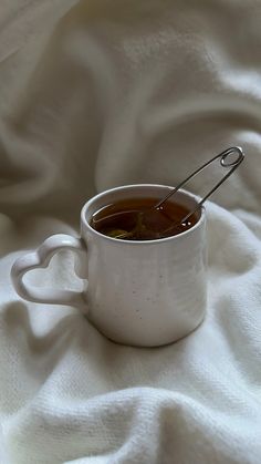 a white cup filled with liquid sitting on top of a bed