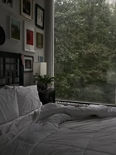 an unmade bed sitting in front of a window with pictures on the wall above it