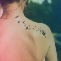 the back of a woman's neck with birds and dandelions on it