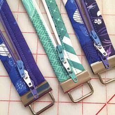 four different colored belts with metal buckles on top of a piece of paper cutting mat