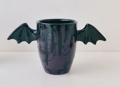 a green cup with black wings on the outside and inside, sitting on a white surface