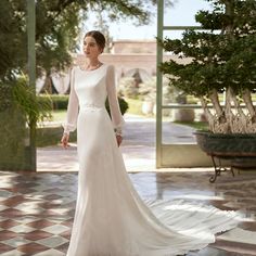 a woman in a white wedding dress standing on a tiled floor with trees and bushes behind her