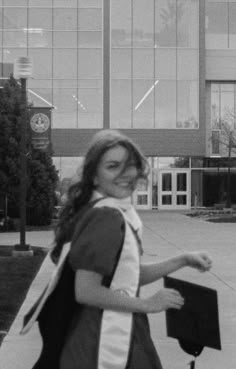 a woman walking down the street with her graduation cap and gown around her neck, in front of an office building