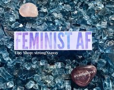 the feminist af sticker is laying on top of some glass rocks and pebbles in front of it