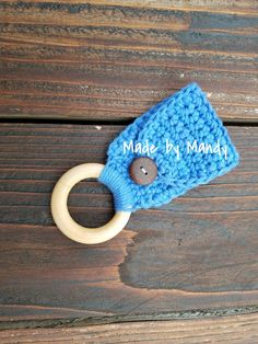 a blue crocheted ring with button on it sitting on a wooden surface next to the word made by mama