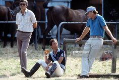 two men sitting on the ground with horses in the background and one man holding a glass of wine