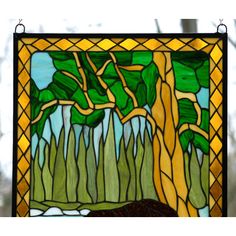 a stained glass window with trees and grass in the background, hanging on a wall