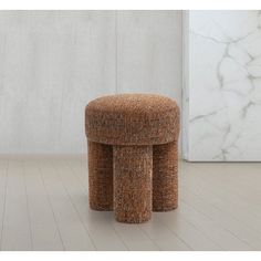 a stool made out of fabric sitting on top of a wooden floor next to a marble wall