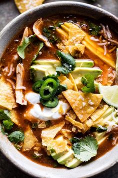 a bowl filled with tortilla soup and topped with sour cream, cilantro, avocado, green onion wedges