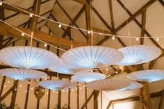 several white umbrellas hanging from the ceiling in a room with wooden beams and string lights