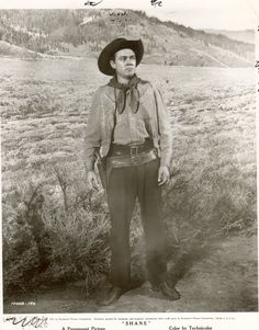 an old black and white photo of a man wearing a cowboy hat standing in a field