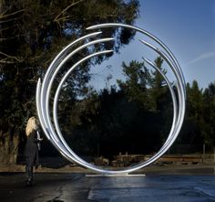 a woman is standing in front of a sculpture that looks like a circular object with four arms