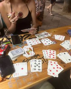 a woman sitting at a table with lots of playing cards on the table and cell phones in front of her