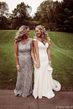 two women standing next to each other in front of a grass covered field and trees