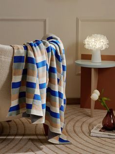 a blue and beige striped blanket sitting on top of a couch next to a vase