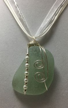 a green sea glass pendant with silver beads on a white necklace cord hanging from a gray surface