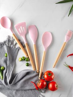 five pink spatulas and some tomatoes on a white marble counter with green peppers