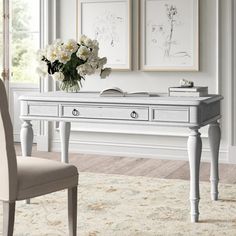 a desk with flowers and pictures on the wall above it in a living room setting