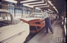 two men standing next to cars on a assembly line