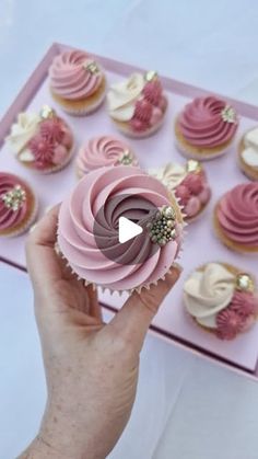 a person holding a pink cupcake in front of many other cupcakes on a table