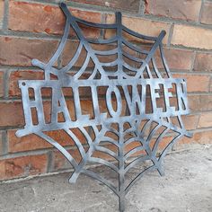 a metal sign that says halloween on it in front of a brick wall with a spider web