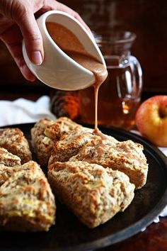 someone is pouring caramel sauce on some scones that are sitting on a plate