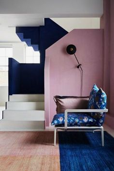 a living room with blue and pink walls, white stairs and a chair in the corner